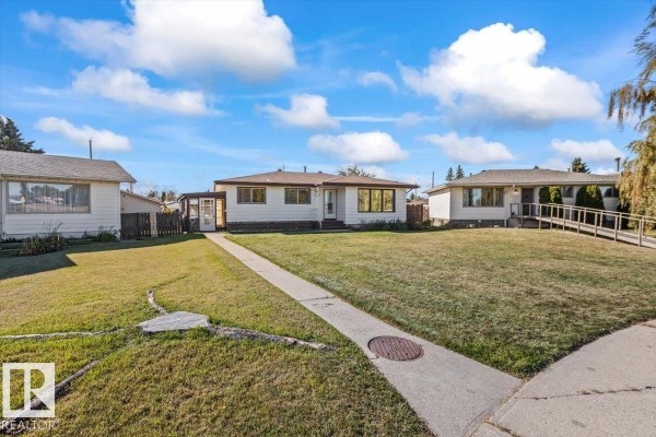 Street view of a white bungalow with a large green lawn and sidewalk. - 7627 128a Av Nw, Edmonton