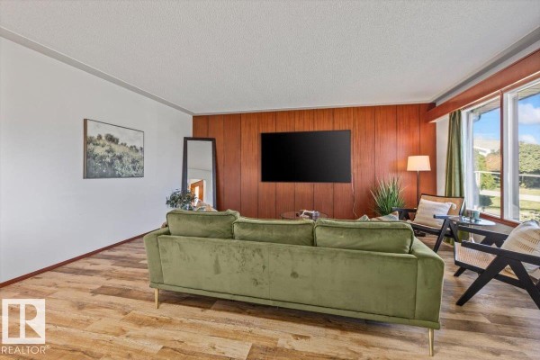 Living room with wood paneling, a green sofa, and large windows. - 7627 128a Av Nw, Edmonton