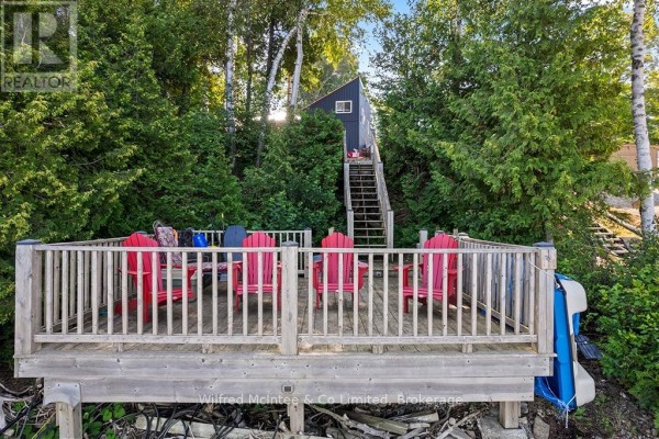 Wooden deck with red chairs, surrounded by trees, with stairs leading up to a small building. - 763 Bruce Road 13, Native Leased Lands
