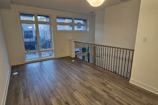 Living area with light wood floors, large windows overlooking the street, and a black railing. - 763 Stanstead Path, Oshawa