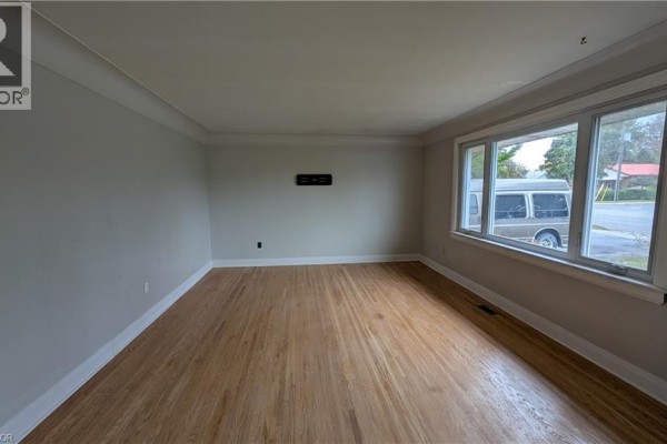 Empty living room with light grey walls, gleaming hardwood floors, and a wide window with exterior view. - 763 Upper Ottawa Street, Hamilton