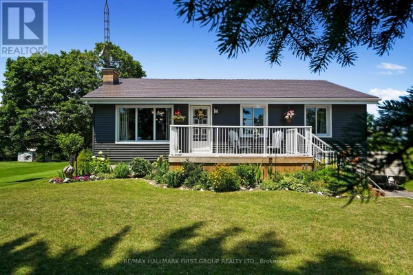 Front facade of a house with dark grey siding, white trim, a wooden deck, and flower beds. - 7638 Telephone Road, Hamilton Township