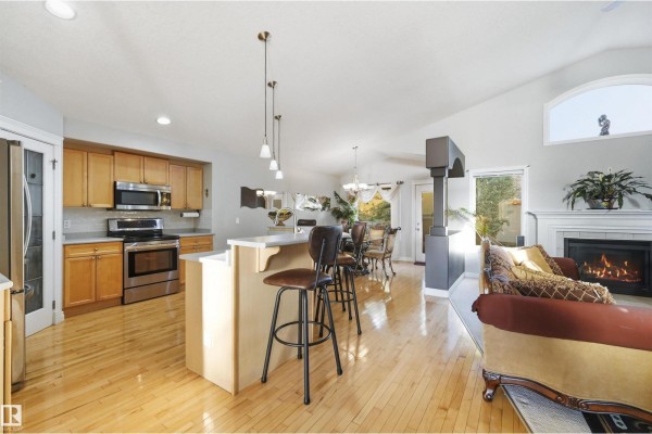 Open concept kitchen and living area with wood floors, a breakfast bar, and fireplace. - 764 Haliburton Cr Nw, Edmonton
