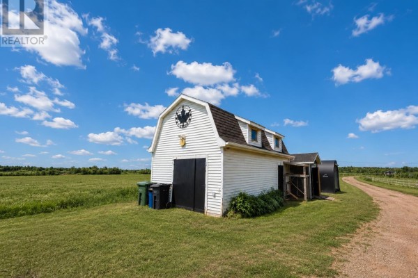 White barn with a dark roof and black doors situated on a grassy field under a blue sky. - 764 Harper Road, Peterville