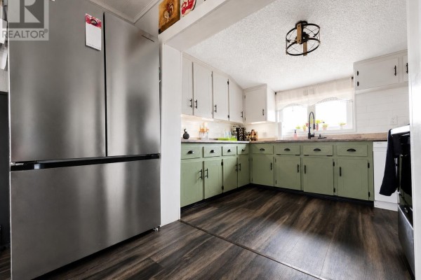Kitchen with stainless steel refrigerator, green lower cabinets, white upper cabinets, and dark wood laminate flooring. - 764 Harper Road, Peterville