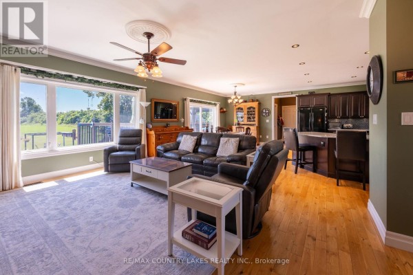 Open concept living and dining area with hardwood floors, leather seating, and a kitchen with dark cabinets. - 764 Regional Road 12, Brock