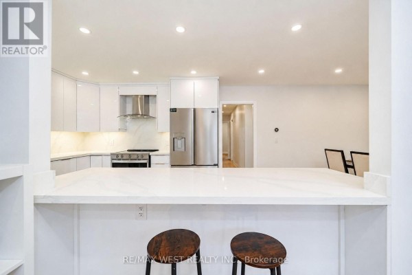View of a bright white kitchen with an island breakfast bar and two stools. - 765 Dodsworth Crescent, Mississauga