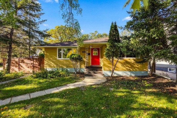 Front exterior of yellow bungalow with red door and stone pathway leading to the entrance. - 765 Oakenwald Avenue, Winnipeg