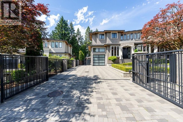 View of a paved driveway leading to a modern grey house with a glass garage door and black metal gates. - 7652 Kerrywood Crescent, Burnaby