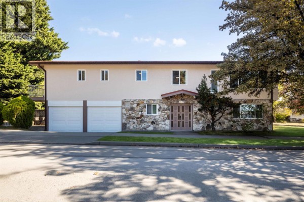 Front facade of a two-story building with a beige stucco exterior, natural stone base, and three garage doors. - 7658 Fremlin Street, Vancouver