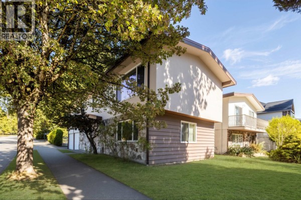 Side view of a two-story residential building with beige and brown siding, large windows, and a manicured lawn. - 7658 Fremlin Street, Vancouver