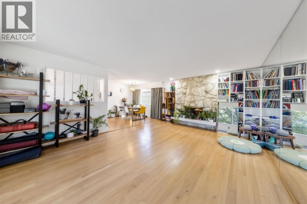 Spacious open-concept room with hardwood floors, a stone fireplace, built-in bookshelves, and a dining area view. - 7658 Fremlin Street, Vancouver