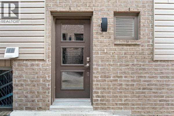 Close-up of the brown front door with glass panels and brick exterior. - 766 Irvine Avenue, Windsor
