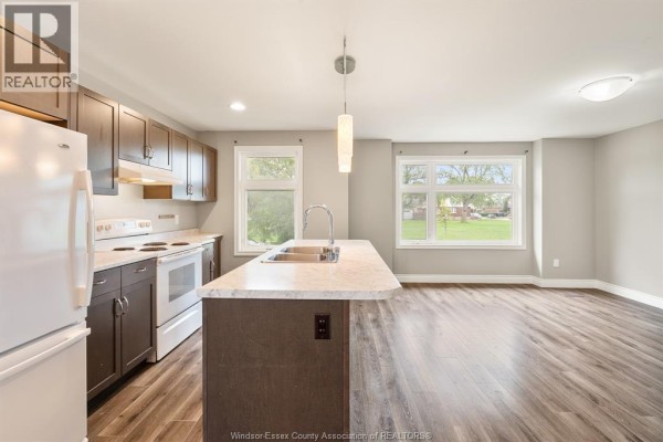 Open concept kitchen with dark cabinets, white appliances, and island in a light gray room. - 766 Irvine Avenue, Windsor