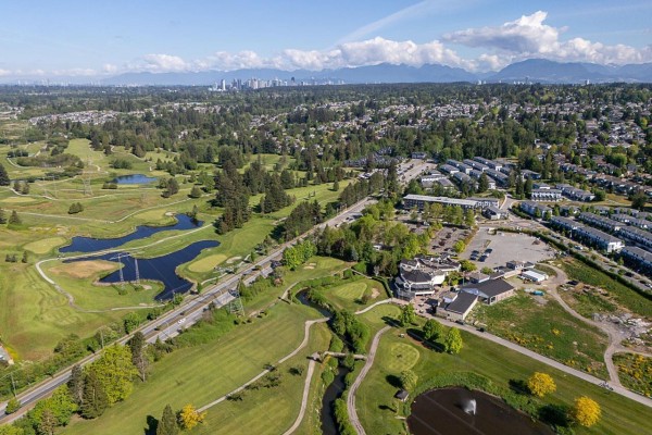 Aerial view of a suburban neighborhood with a golf course and distant city skyline. - 7667 155 Street, Surrey