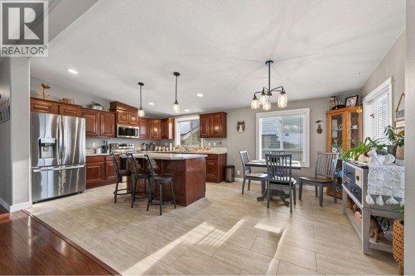 Open concept kitchen with dark wood cabinets, granite countertops, island, and dining area. - 768 Shuswap  E Road Unit# 14, Kamloops