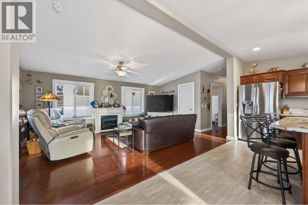 Living room with a fireplace, brown leather sofa, recliner, and adjacent kitchen island. - 768 Shuswap  E Road Unit# 14, Kamloops