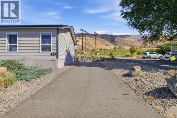 The side of a light gray mobile home with a paved driveway and rocky landscaping. - 768 Shuswap  E Road Unit# 24, Kamloops