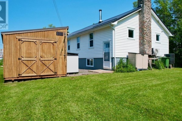 Rear exterior of the house with white siding, a large wooden shed, and green lawn. - 7682 6 Highway, Port Howe
