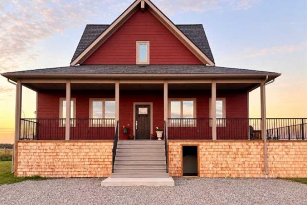 Front view of a red house with a covered porch, stairs, and natural wood siding on the foundation. - 77, 210044 Highway 512, Rural Lethbridge County