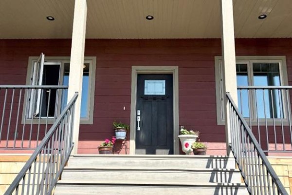 Close-up view of the front door and steps of a red house, flanked by windows and potted plants. - 77, 210044 Highway 512, Rural Lethbridge County