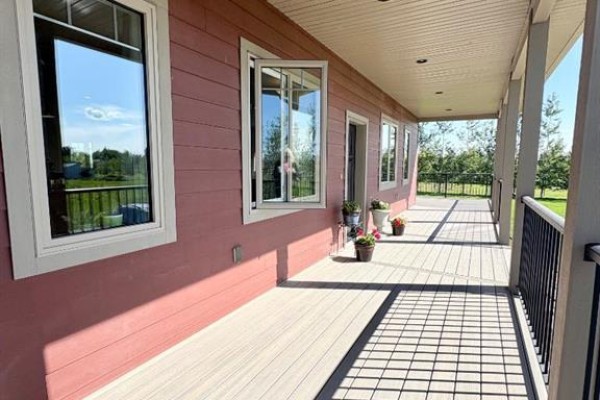 View of a covered porch with composite decking, railings, and windows on the exterior of a red house. - 77, 210044 Highway 512, Rural Lethbridge County