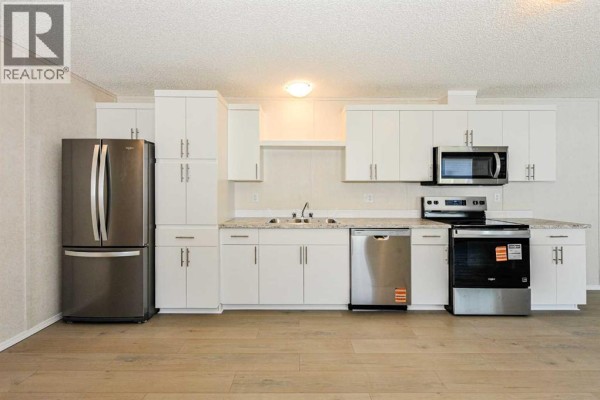 Modern kitchen with white cabinets, stainless steel appliances, and wood-look flooring. - #77, 4802 54 Avenue, Camrose