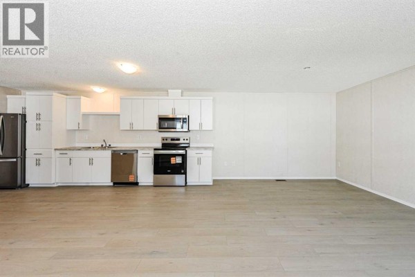 Open-concept living area and kitchen with white cabinets and light wood flooring. - #77, 4802 54 Avenue, Camrose