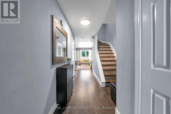 Hallway with light blue walls, hardwood floors, leading to a living area and stairs. - 28 - 3395 Cliff Road N, Mississauga
