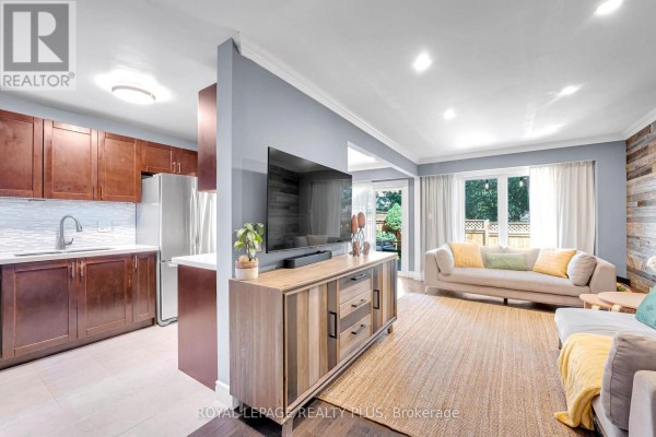 Open concept living area and kitchen with a sectional sofa, mounted TV, and dark wood cabinets. - 28 - 3395 Cliff Road N, Mississauga