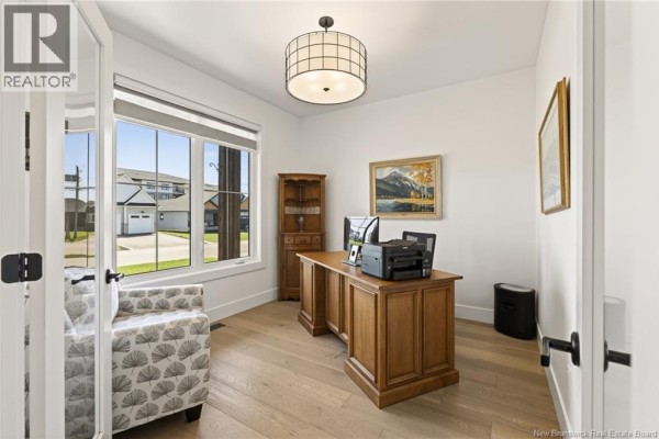 Home office with a large window, wooden desk, chair, and floor-to-ceiling shelving unit. - 77 Bouchard Street, Dieppe