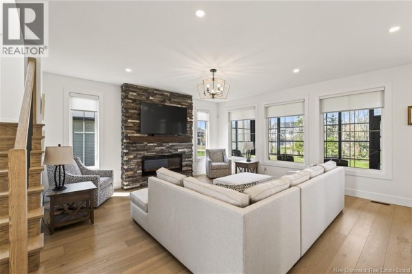 Spacious living room with a sectional sofa, stone fireplace, large windows, and hardwood floors. - 77 Bouchard Street, Dieppe