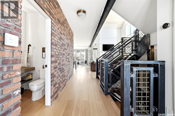 Hallway with exposed red brick wall, staircase with metal railings, and light wood floors. - 77 Deer Foot Trail, Lumsden Rm No  189