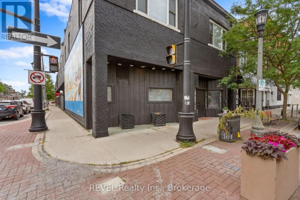 Close-up of a commercial building's black exterior with glass doors and planters. - 77 East Main Street S, Welland