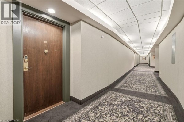 Apartment building hallway with patterned carpet, beige walls, and multiple apartment doors. - 77 Governor's Road Unit# 404, Dundas