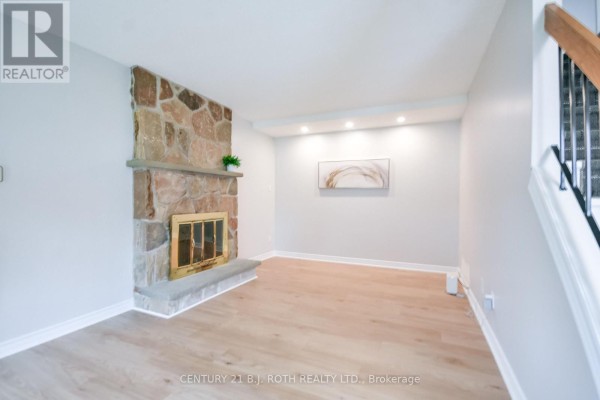 Living room featuring a floor-to-ceiling stone fireplace with a brass grate and light wood flooring. - 77 Pepler Place, Barrie