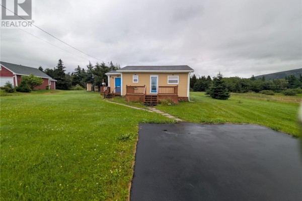 View of the beige house from the driveway, with green grass and trees surrounding it. - 77 Point Au Mal Road, Point Au Mal