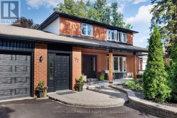 Facade of a two-story red brick house with a covered porch and large trees. - 77 Sanderling Crescent, Kawartha Lakes