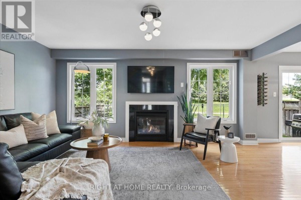 Living room with a black leather sofa, gas fireplace, and large windows overlooking a green backyard. - 77 Shoniker Drive, Newmarket