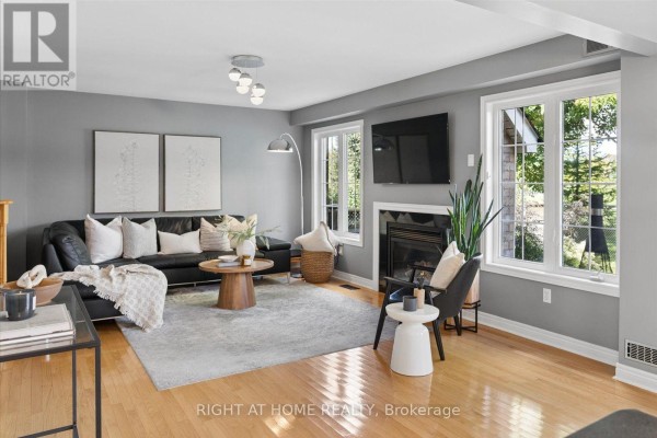 Living room with a black leather sofa, gas fireplace, and windows showing trees and backyard view. - 77 Shoniker Drive, Newmarket