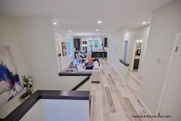 Open-concept main floor with light wood-look flooring, white walls, and a view of the living and kitchen areas. - 77 Spruce Cove, West St Paul