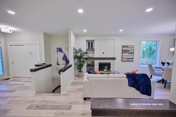 View of the open-concept living area with a white sofa, fireplace, and dining area leading to the backyard. - 77 Spruce Cove, West St Paul