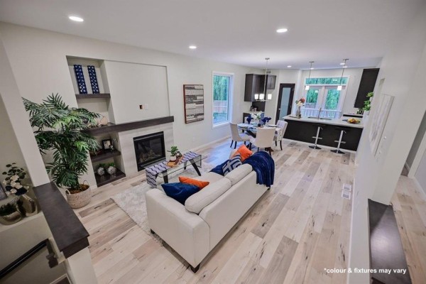 Spacious living room with white sofa and coffee table, adjacent to a dark-cabinet kitchen with island seating. - 77 Spruce Cove, West St Paul