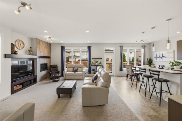 Open-concept living and dining area with a fireplace, white sofas, and a breakfast bar. - 77 Tackaberry Way, Winnipeg