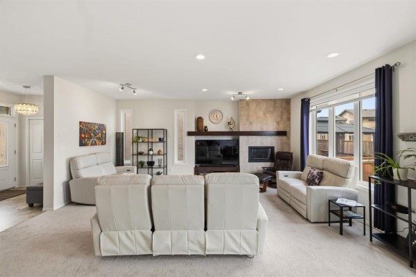 Living room showing white sofas, a fireplace with stone accent wall, and a sliding glass door. - 77 Tackaberry Way, Winnipeg