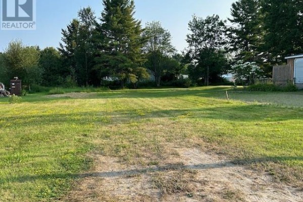 Grassy area with a gravel section, bordered by trees and nearby buildings. - 77 Togo St, Blind River
