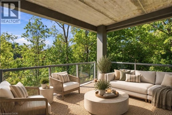 Covered balcony with sectional sofa, armchairs, and coffee table with green treetop views. - 77 Yates Street Unit# 201, St  Catharines