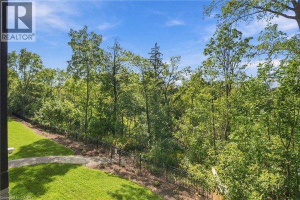 View of lush green trees and grass with a black metal fence and paved path. - 77 Yates Street Unit# 201, St  Catharines