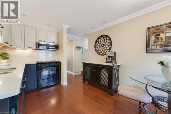 Kitchen with dark blue lower cabinets, white uppers, black stove, and hardwood floors. - 77 Yellow Birch Drive, Kitchener