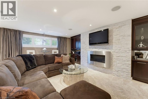 Basement family room with a sectional sofa, mounted TV, fireplace, and dark wood built-ins. - 77 Yellow Birch Drive, Kitchener